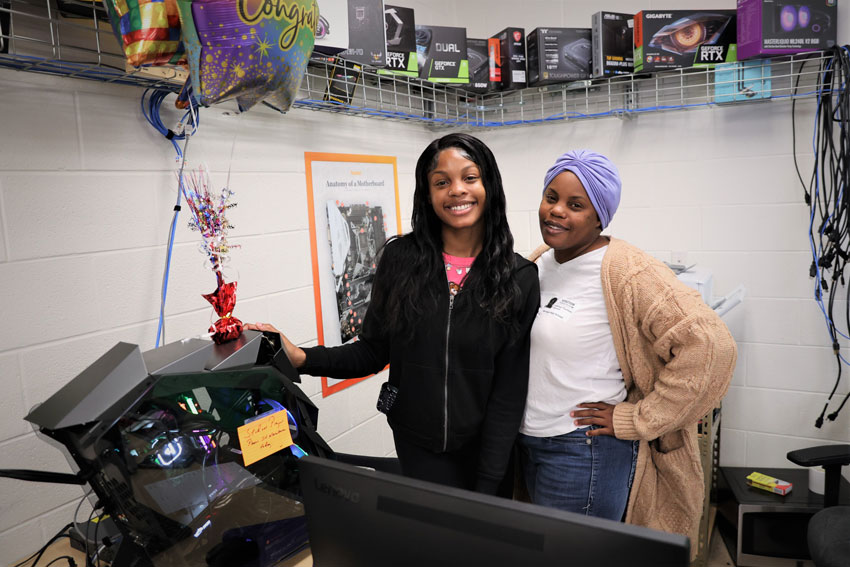 Daughter and mother standing next to computer in classroom