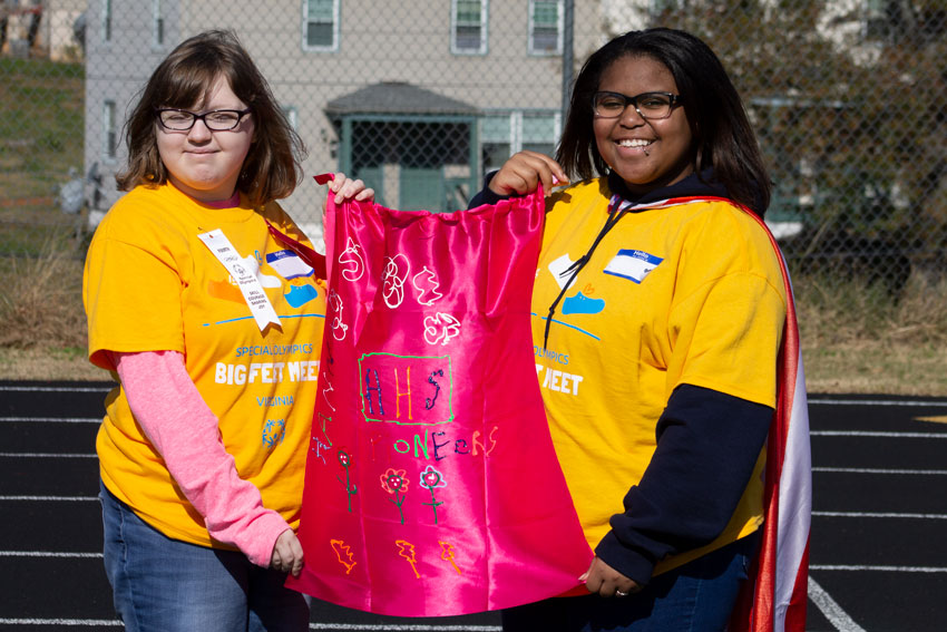 Two female students in matching shirts holding cape with handwritten message