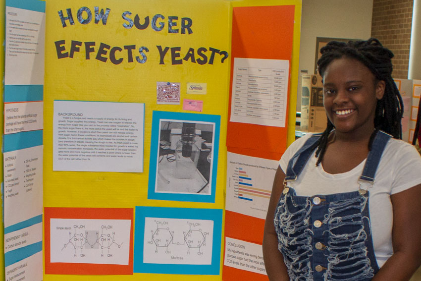 Student next to science fair project titled "How Sugar Effects Yeast"