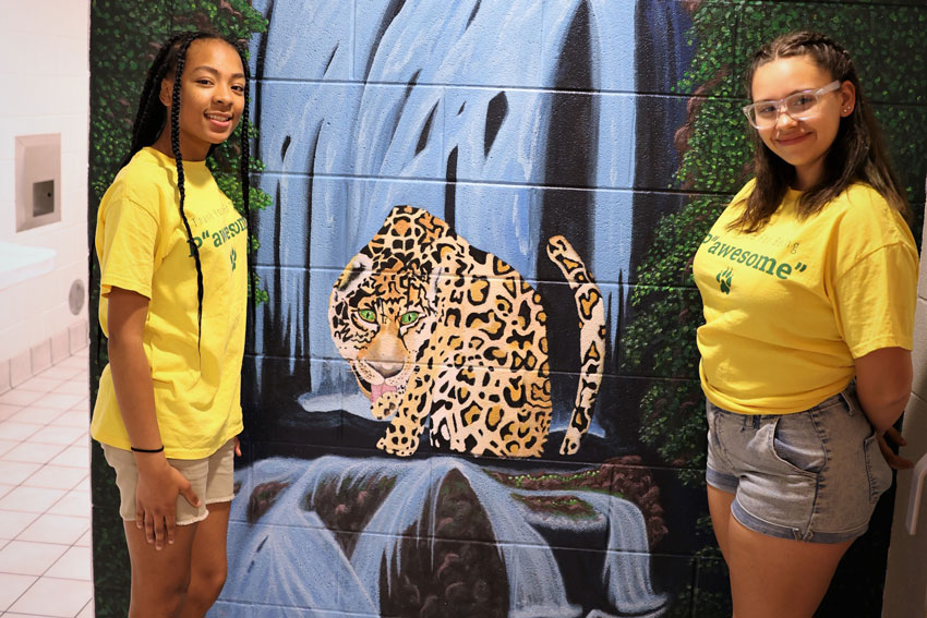 2 girls standing in front on mural