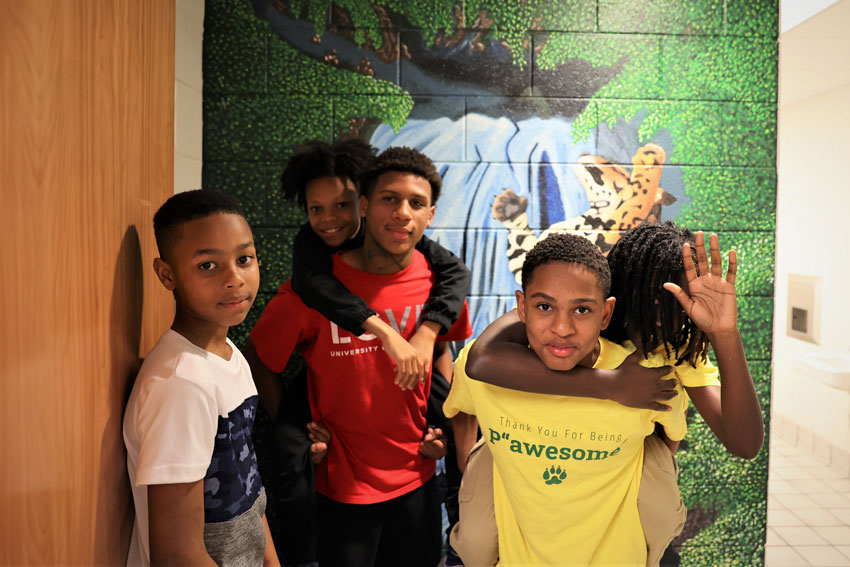 5 boys standing in front on mural