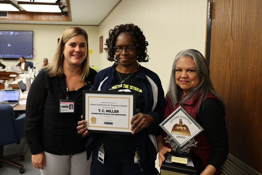 Two custodians with school principal holding awards 