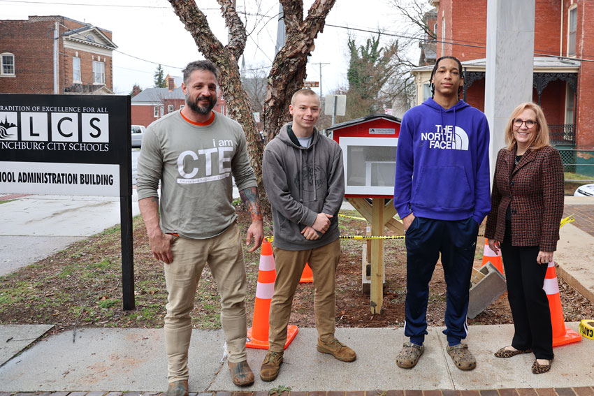 Carpentry teacher with two students and administrator in front of recently installed Little Free Library