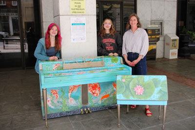 Teacher and two students standing with painted piano