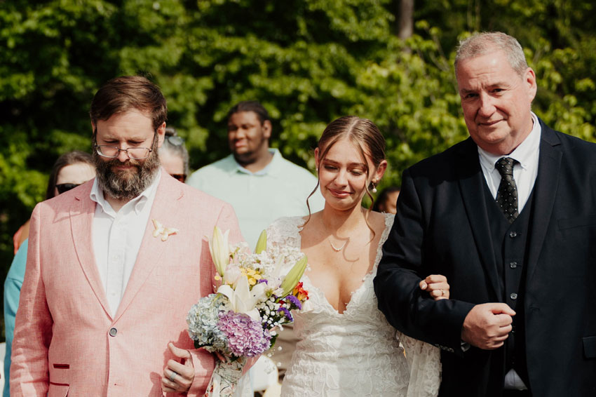 Two men walking bride down the aisle at outdoor wedding