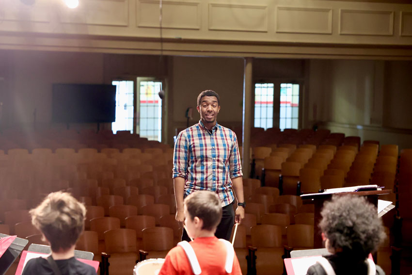 Music teacher directing elementary drumline practice in auditorium