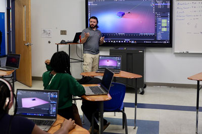 Teacher talking to class in front of display with 3D rendering software