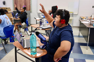 Student with podcast equipment raising hand 
