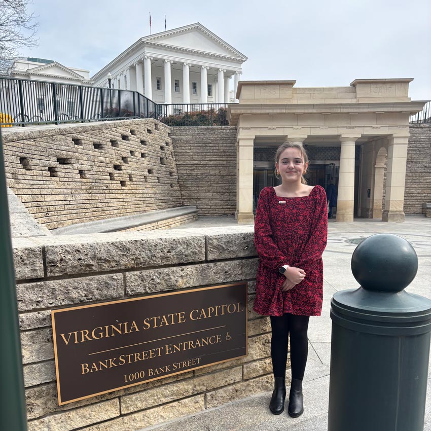 Eve Flavin standing next to Virginia State Capitol entrance sign