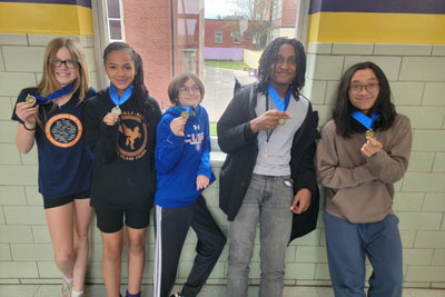 Five students showing off medals in the hallway at Dunbar Middle School