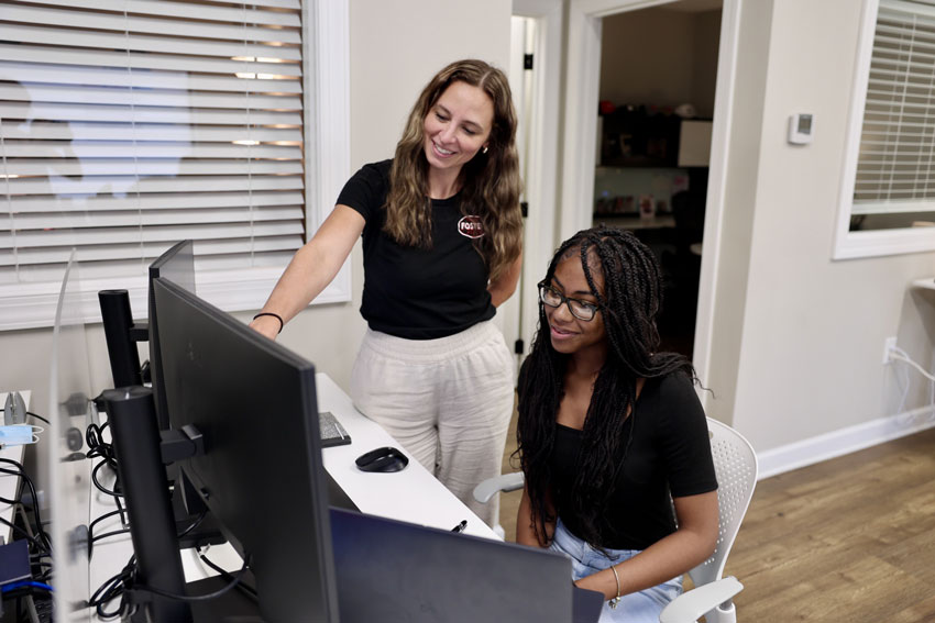 Student seated with woman in Foster Fuels shirt pointing at computer