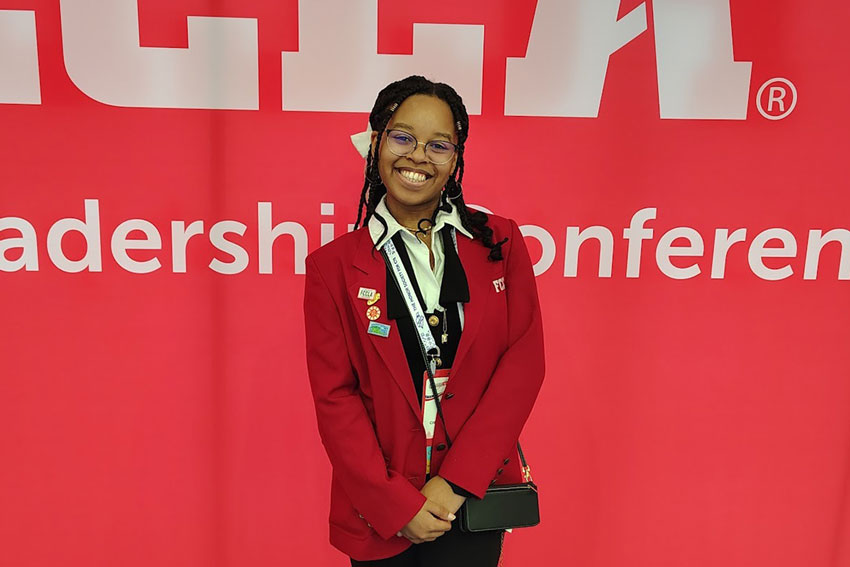  Jasmine Ford in red blazer standing in front of FCCLA National Leadership Conference backdrop