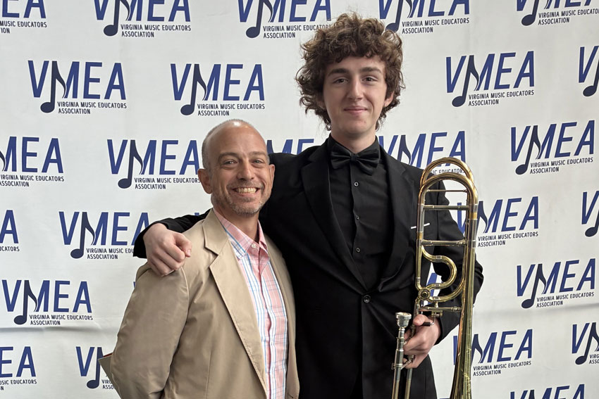 Band Director Brown and trombonist Alton Quinn standing in front of Virginia Music Education Association (VMEA) backdrop