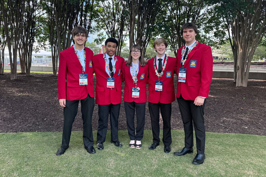 Five students wearing event credentials and matching red blazers posing together outside