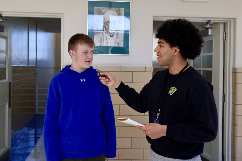 Student interviewing another student in school hallway