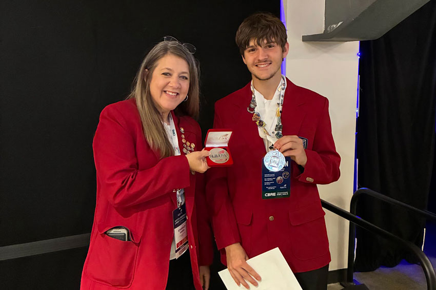 Teacher and student in matching red blazers holding awards backstage at national competition