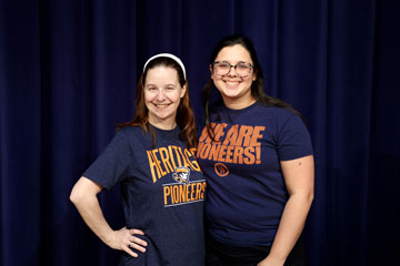 Erin Foreman and Taylor Wisskirchen standing in front of stage curtain wearing Heritage High School shirts
