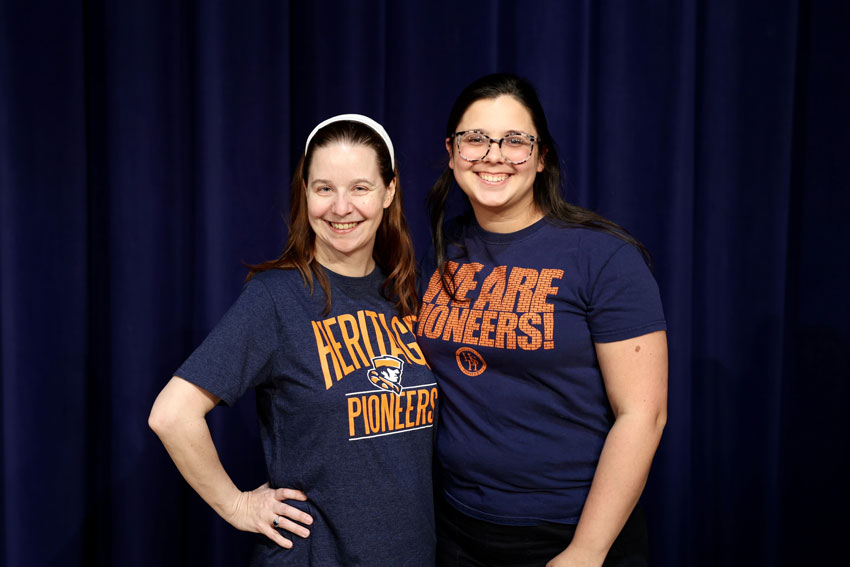Erin Foreman and Taylor Wisskirchen standing in front of stage curtain wearing Heritage High School shirts