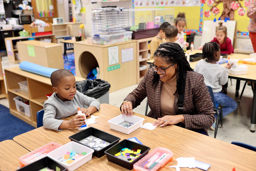 Superintendent working on craft at table with preschool student holding bottle of glue
