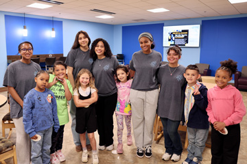 5 college students in matching shirts with 6 smiling elementary students