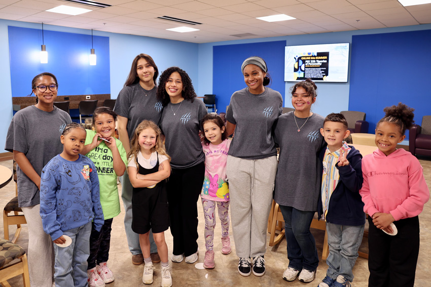5 college students in matching shirts with 6 smiling elementary students