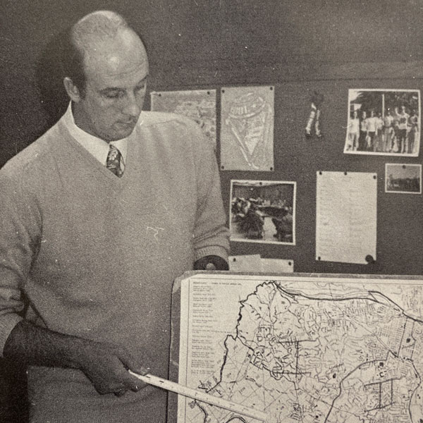 Black and white photo of principal pointing to neighborhood map
