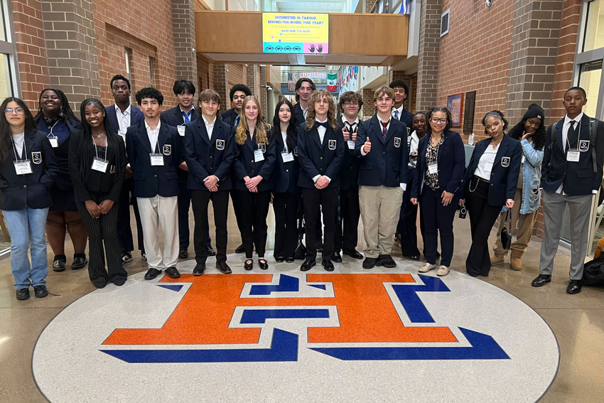 Large group of DECA students with teacher in main hallway at Heritage High School
