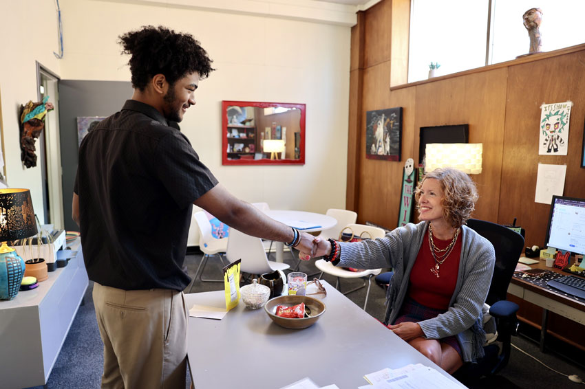 Student shaking hands with woman seated at desk