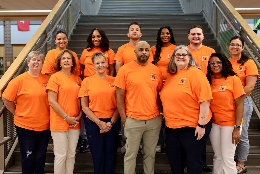 Group of school staff in matching orange shirts standing on stairs