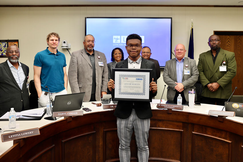 Scholarship recipient holding certificate in front of School Board members in Board Room