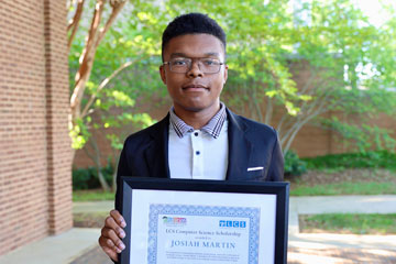 Joey Martin holding scholarship certificate in front of School Administration Building