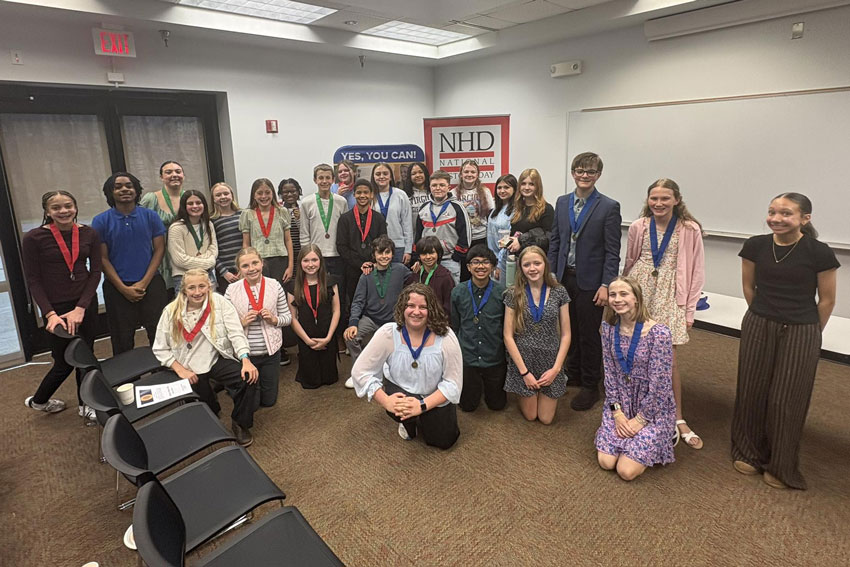 Large group of students at competition wearing medals, National History Day banner in background