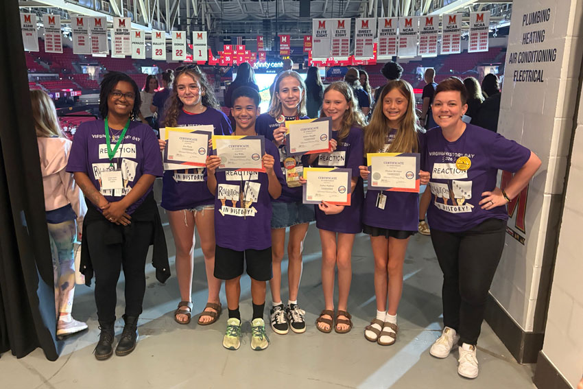 Students and teachers in matching t-shirts standing in arena, with students holding certificates