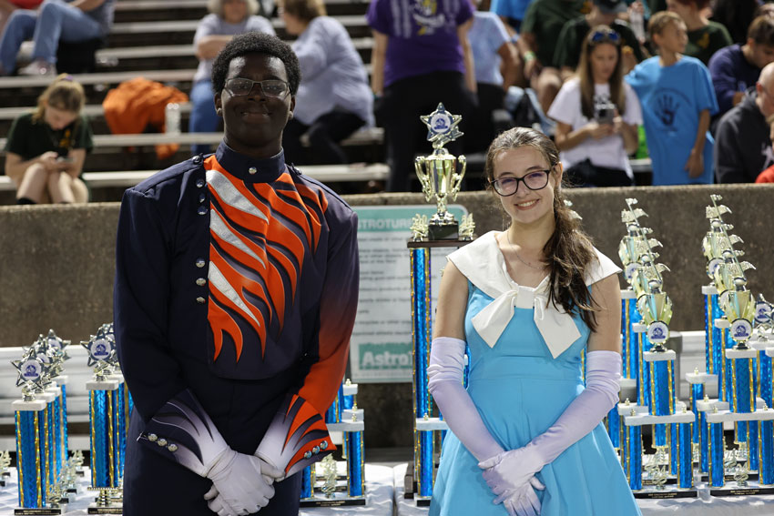 Two marching band drum majors standing in front of table full of trophies
