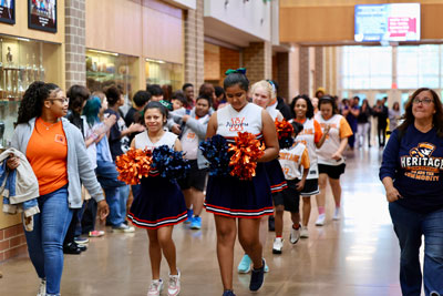 Cheerleaders and basketball players walking down hallway surrounded by fellow students