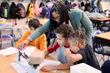 Superintendent with three boys using scale to complete classroom project