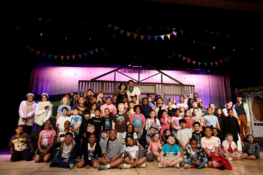 Large group of elementary students and high school drama students in costume on stage