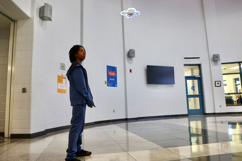 Student flying drone in school lobby area