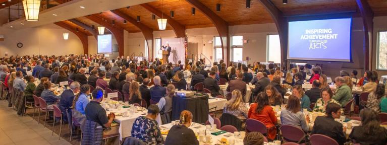Full room of participants seated for meal in event space