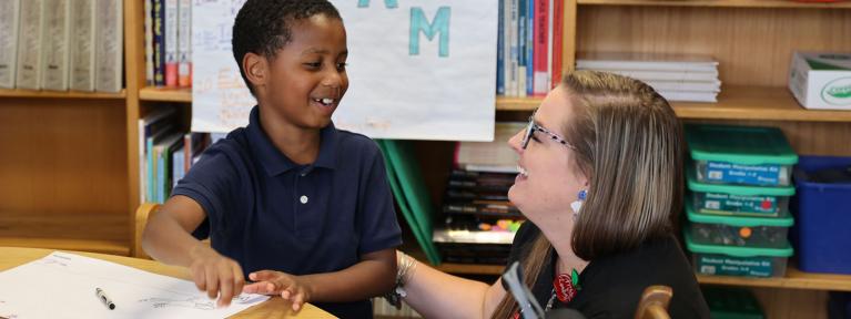 Smiling teacher kneeling next to student