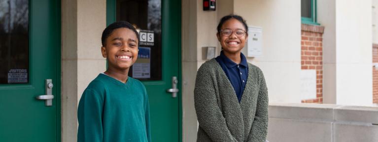 Two smiling students on the steps in front of school