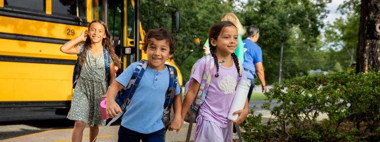 Three happy students walking into school from the bus