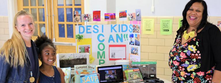 Two teachers with student in front of grant display