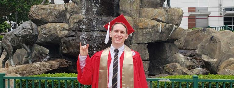 Student in college cap and gown in front of fountain