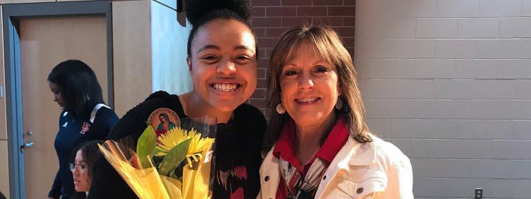 Smiling student holding flowers standing with foundation representative