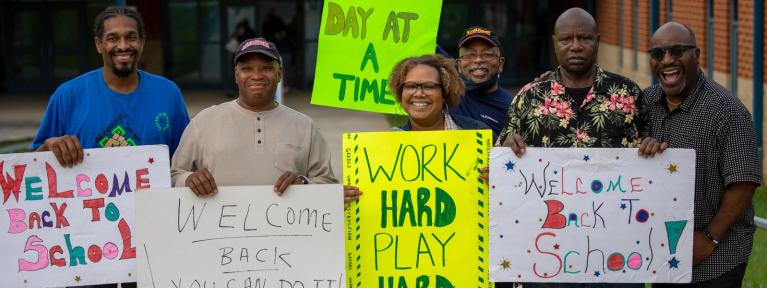 Volunteers outside school holding encouraging signs