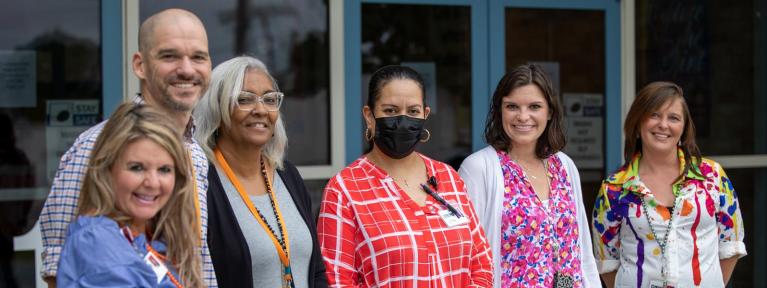 Smiling faculty and staff standing outside school