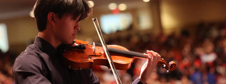 Student playing violin with audience in background