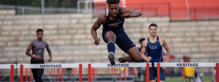 Boy jumping hurdle during race