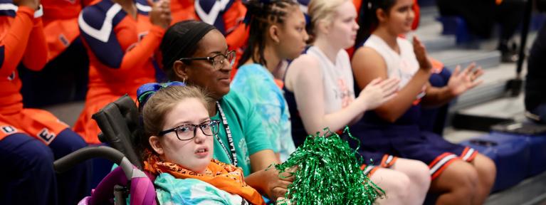 Student with pom-pom watching Medford League game with staff and classmates